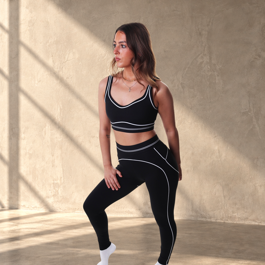 Model wearing Lanula Outline Leggings and matching sports bra in black with white contour piping on white background