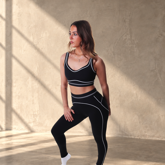 Model wearing Lanula Outline Bra and matching leggings in black with white contour piping against a white background