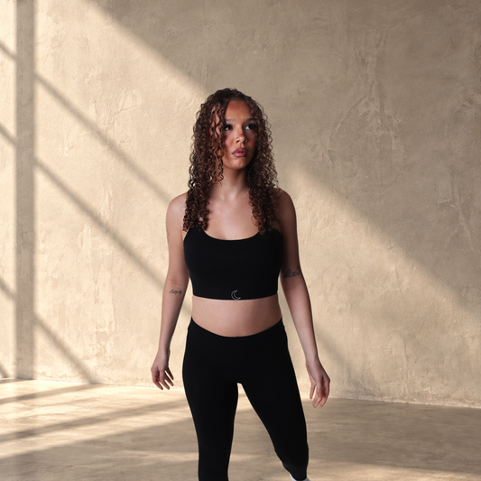 Model wearing a black Lanula ESSENCE bra and matching leggings, featuring a minimal design and soft stretch fabric.